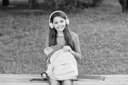 Audiobook education. Student girl. School education. Student life. School girl listen audiobook in headphones outdoor. Back to school. Education and knowledge. Girl listening to audiobook with bookの写真素材