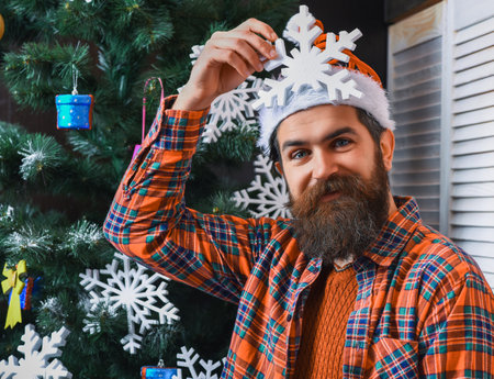 Santa man with moustache. Christmas tree at home. Brutal man celebrate Xmas. Merry Christmas. Santa Claus bearded man. Happy New 2025 Year. Xmas holiday celebration. Snowflake decorationの写真素材