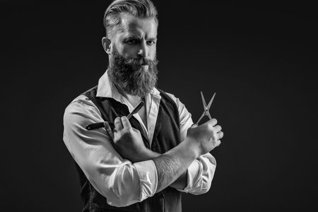 Man beard haircut by hairdresser at barbershop. Handsome barber using retro blade and scissors while cutting hair. Modern barbershop haircut. Bearded hipster barber isolated on blackの写真素材