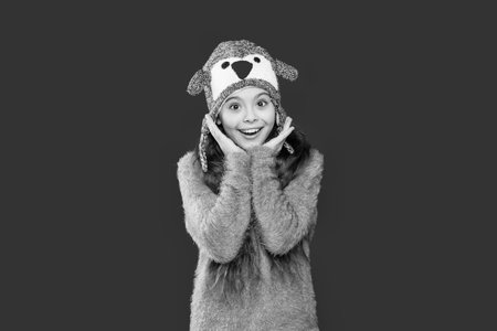 Winter girl child. Style portrait of teen girl in warm clothing and winter hat isolated on red. Knitted sweater and beanie hat. Trendy fashion outfit in winter. Winter activityの写真素材