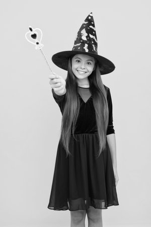 October 31. Teen girl in witch costume hold magic wand. Happy Halloween. Girl witch in Halloween costume isolated on yellow. Trick or treat. All Hallows party. All Hallows witch. Spooky treatsの写真素材