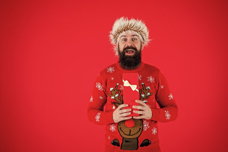 Santa Claus man in hat and Christmas sweater hold Xmas present or gift for new year holiday isolated on redの写真素材