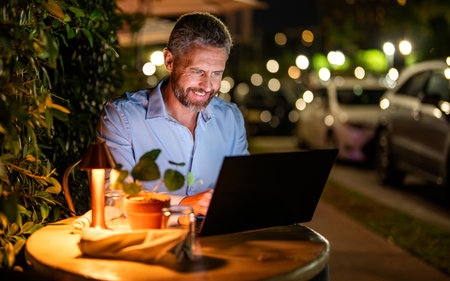 Successful businessman freelancing online. Business success. Businessman working on laptop outdoor. Business man having video laptop call in the evening cafe. Business man working online, copy spaceの写真素材