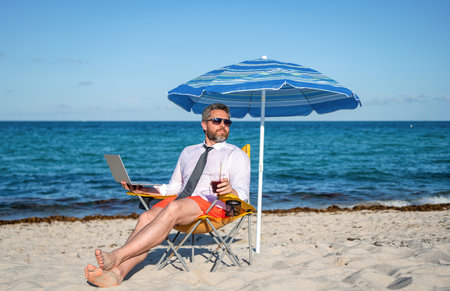 Online freelance. Businessman remote with laptop. Business man using laptop in beach. Travel and business. Man freelance online at sea beach. Businessman on summer vacation. Digital nomad lifestyleの写真素材