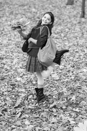Autumn fall leaves. Knowledge and education. Knowledge day. School education. Autumn girl in uniform hold fall leaves outdoor. Stylish teen girl at school break. Back to school. Childhood happinessの写真素材