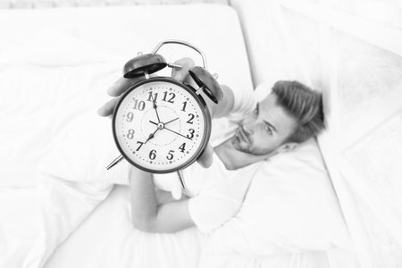 Time to wakeup and get up. Morning wakeup. Sleepy man with alarm clock in hand lying in bed. Morning...