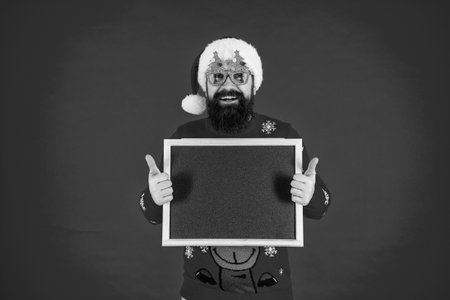 Santa Claus bearded man in hat and Christmas sweater hold Xmas advertisement for new 2024 year winter holiday isolated on redの写真素材