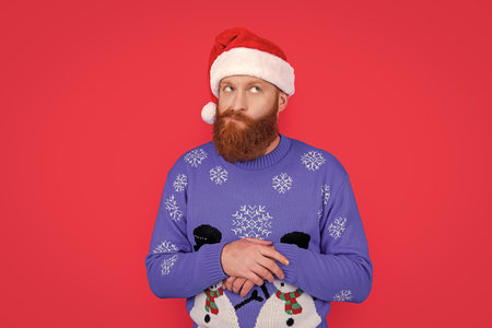 caucasian wondered man in new year sweater and santa hat isolated on red background.の写真素材