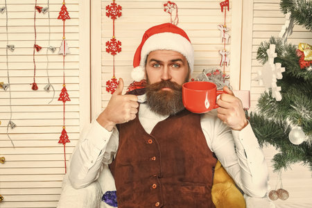 Santa man in retro style with mug. Delicious cocoa for Christmas. Man celebrate Xmas. Merry Christmas. Santa Claus retro man drinking coffee. Happy New 2025 Year. Xmas holiday celebration. Thumb upの写真素材