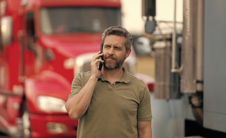 Truck driver has phone call. Trucking owner. Transportation vehicles. Hispanic man posing in front of truck. Semi trucks vehicle. Man owner truck driver. Man driver talking on phone near lorry truckの写真素材