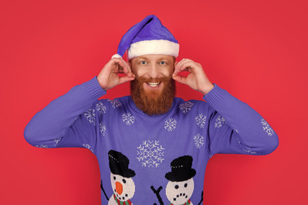 Bearded man in Santa wear twisting mustache studio. Happy Santa Claus twirling moustacheの写真素材