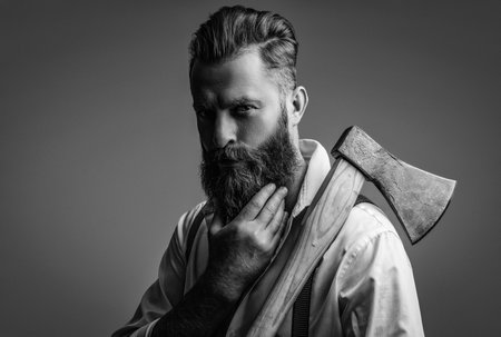 Brutal mature bearded man with redhead beard and moustache in retro suspenders hold axe isolated on greyの写真素材