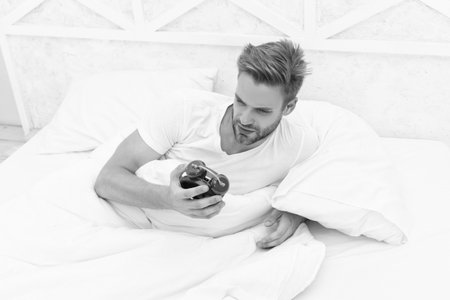 Time to wakeup and get up. Morning wakeup. Sleepy man looking at alarm clock in hand while lying in bed. Morning awakening. Sleepy man turning off alarm clock. Waking up early. Turns off Alarm Clockの写真素材