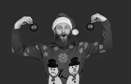 Xmas holiday celebration. Santa man at New Year. Winter holiday for man in Santa hat. Xmas sweater. Man with decoration isolated on red. Merry Christmas. Happy New Year. New beginningsの写真素材