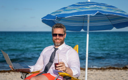 Man freelance work online at sea beach. Businessman on summer vacation. Online freelance marketing. Businessman remote worker with laptop. Business man using laptop in beach. Travel and businessの写真素材