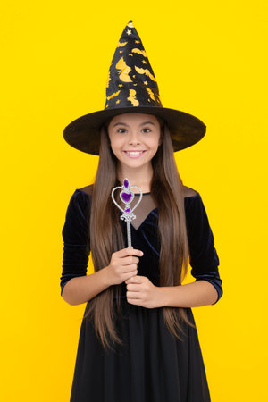 All Hallows party. All Hallows witch. October 31. Teen girl in witch costume hold magic wand. Happy Halloween. Girl witch in Halloween costume isolated on yellow. Trick or treat. Mystical wandの写真素材