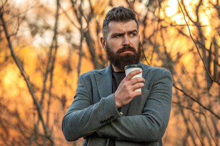 Everyday style routine. Bearded man having coffee in autumn city. Fall man in park with coffee cup....