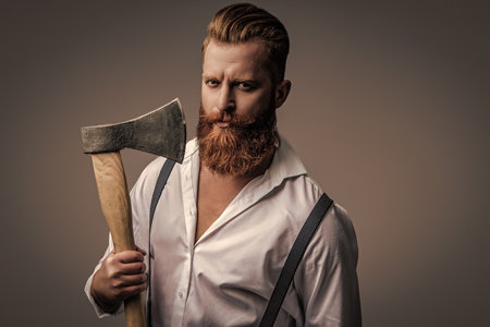 Brutal bearded man in vintage suspenders holding ax isolated on grey