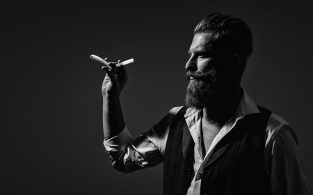 Handsome barber using retro blade while cutting hair. Modern barbershop haircut. Bearded hipster...