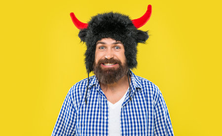 Brutal man wearing bull hat isolated on yellow. Bearded man in party hat. Bearded and brutal...