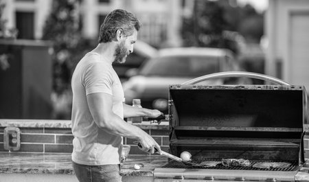 man preparing grilled food at backyard barbecue. man with hot grill at a barbecue party. Expert grill chef. man grilling delicious barbecue on a summer dayの写真素材