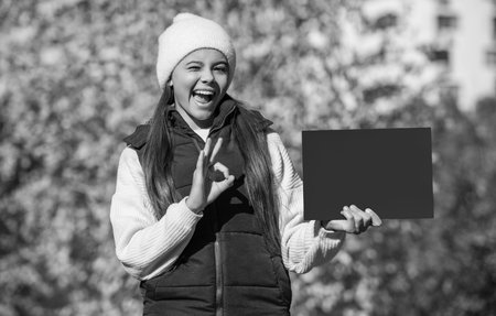 suggestion concept. winking teenager girl suggest something on paper with copy space. autumn girl make a suggestion. girl suggest fall season sale. suggest for this autumn. fall time advertisementの写真素材