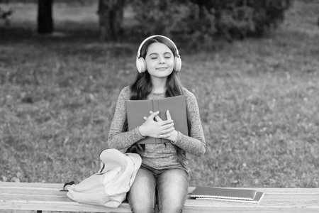 Audiobook vs book. Student girl feel inspired. School education. School girl read book and listen audiobook outdoor. Back to school. Education and knowledge. Girl listen audiobook and read bookの写真素材