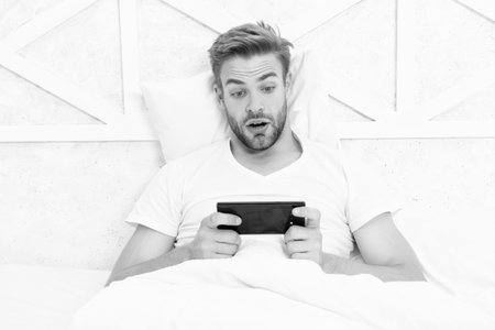 Video gaming online. Man watching phone. Man betting in bedroom. Video call. Millennial guy at...