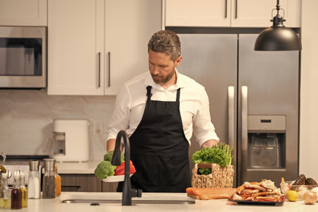 Man cook food in modern kitchen. Cooking healthy salad. Chef cooking in apron. Man cook cooking at...