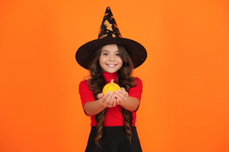 Costume party. Halloween pumpkin in hand of witch girl. Halloween witch girl isolated on orange....