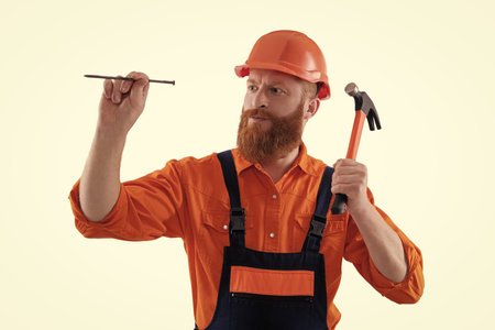 Man hold hammer nail. Carpentry and repairing. Repairman in uniform has hammer. Bearded repairman...