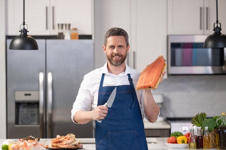 Seafood cuisine. Cooking healthy food. Chef man hold trout fish fillet. Man cook trout in apron. Cooking fish at home. Mature professional man cook trout fillet. Fried fishの写真素材