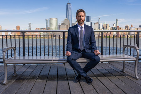 Hispanic businessman resting and meditating. Healthy yoga meditation after work. Zen businessman meditating at city skyline. Successful man meditate. Meditation of man in business suit outdoorの写真素材