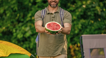 Man with watermelon in summer camping. Man hiker outdoor on summer day. Summer camp and nature picnic. Man on summer camping. Camp watermelon food. Yummy healthy food. Fresh food in campの写真素材