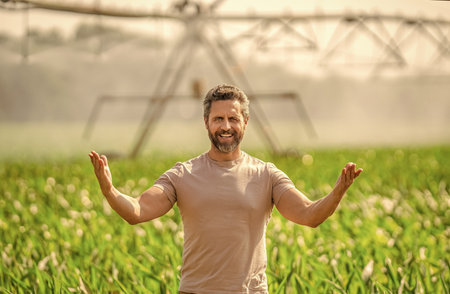 Drip irrigation system. Crop irrigation. Agriculture and farming. Man at irrigation system watering agricultural field. Farmer man presenting result. Water sprinkler irrigating crop fieldの写真素材