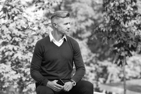 Businessman in autumn park. Caucasian man has business casual style. Mature man use mobile phone....