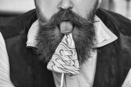 Xmas holiday celebration. Bearded man at New Year eve. December holiday party for man has moustache, cropped view. Xmas man licking candy lollipop. Christmas candy. Merry Christmas. Happy Ney Yearの写真素材