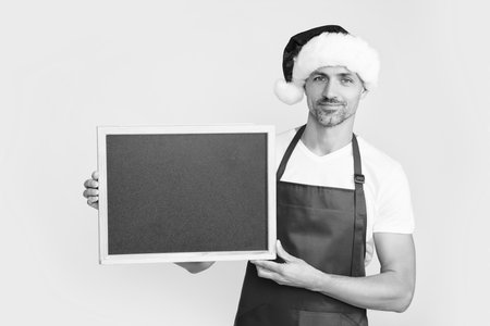 cheerful mature man in santa hat and apron hold blackboard with copy spaceの写真素材