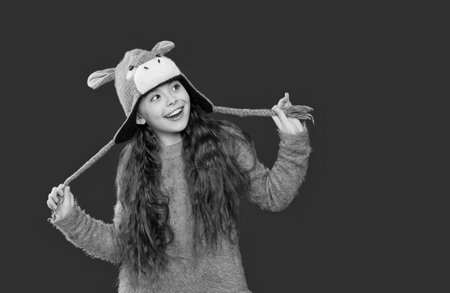 Outdoor lifestyle fashion. Teenager girl in a winter warm hat isolated on red. Happy girl in winter hat. Winter fashion style. Teenager knitted fashion. Childhood innocenceの写真素材