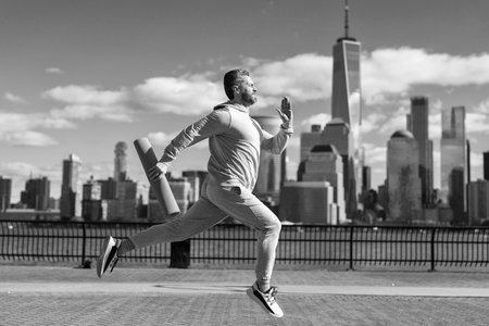 Sportsman in activewear training jogging running in New York with fitness mat for workout outdoor