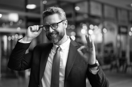 Happy successful businessman man in suit and glasses showing ok gesture outdoor at business officeの写真素材