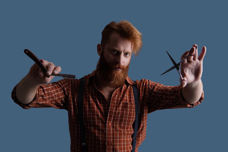 Man with long red beard. Hairstylist at barber shop isolated on grey. Barber using scissors and retro blade. Hairstylist cutting at barber shop. Barbershopの写真素材