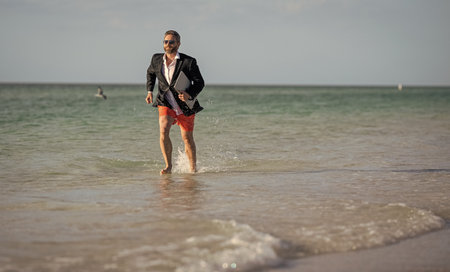 Businessman in suit with laptop running in sea. Businessman running at summer vacation. Business success of businessman, copy space.の写真素材