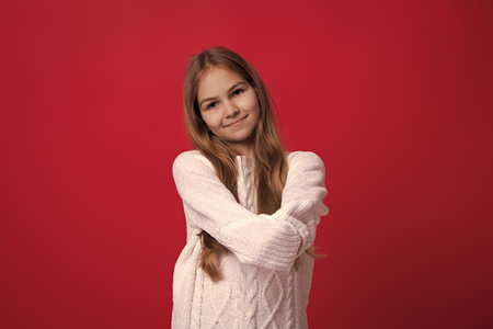 Winter fashion style. Girl in knitwear. Portrait of teen child wearing warm winter clothes. Girl kid wear warm sweater isolated on red. Happy stylish childhood. Teen girl in sweater. Cozy lookの写真素材