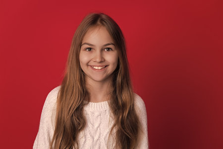 Knitted sweater. Teen girl wearing stylish sweater. Childhood winter memories. Teen girl kid isolated on red studio. Child winter fashion. Girl enjoying winter style. Happy childhoodの写真素材