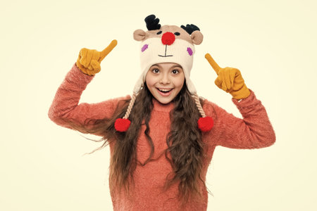 Girl in knitwear. Portrait of teen child wearing warm winter clothes. Girl kid wear warm hat isolated on white. Happy childhood. Teen girl in earflap hat. Winter fashion style. Point fingerの写真素材