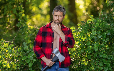 Strong man work in forest. Man in forest with axe. Lumberjack carries axe. Mature sweating man with...