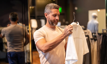 Male fashion shop. Stylish man in menswear boutique. Mature man choosing tshirt. Designer clothing....