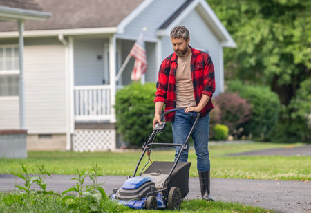 Backyard grass maintenance. Hispanic gardener. Lawnmower mow the green grass. Man gardener cut the...