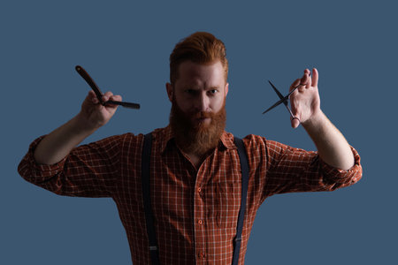 Hairstylist at barber shop. Barbershop. Man with long red beard. Hairstylist at barber shop isolated on grey. Barber using scissors and retro blade. Hairdresser cutting hair. Quick trimの写真素材